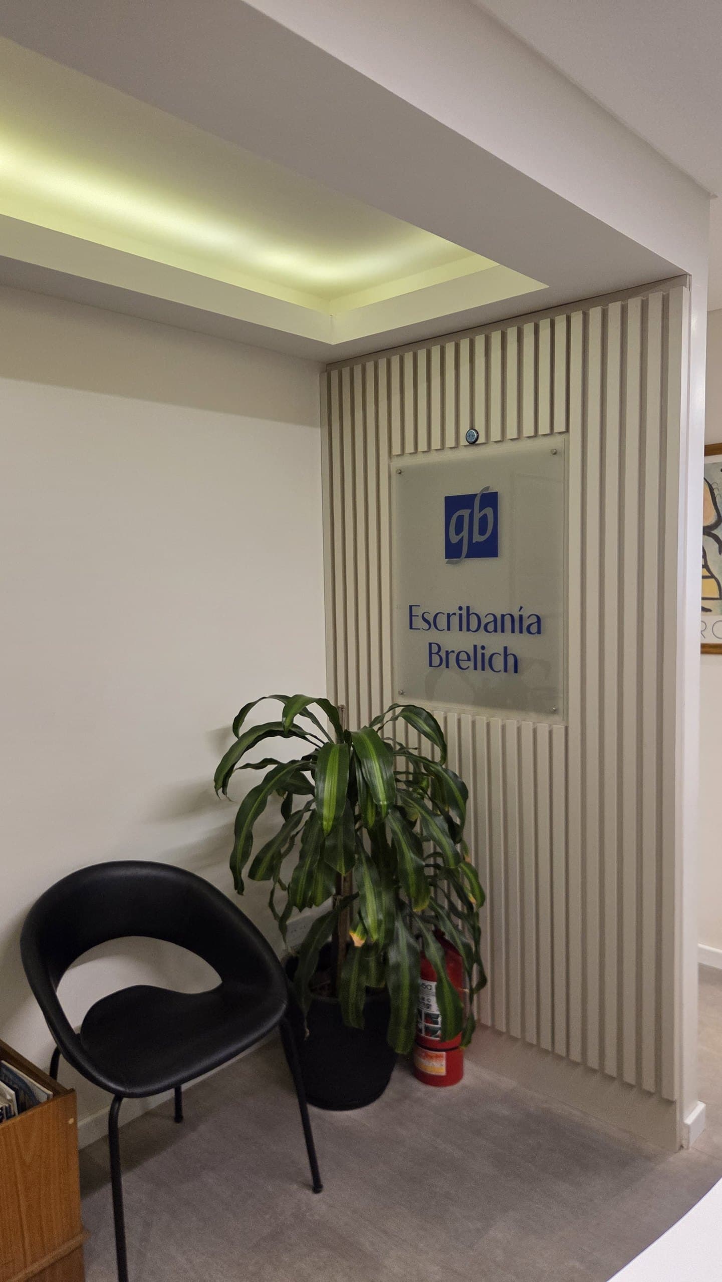 La recepción del estudio: el cartel con el «gb» y el nombre Escribanía Brelich sobre la pared de listones, junto a una planta.